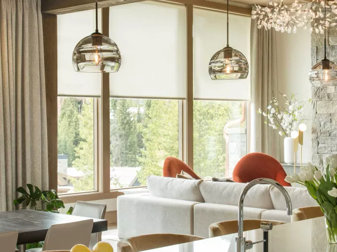 Layered window treatments featuring motorized roller shades and drapes with decorative light fixtures