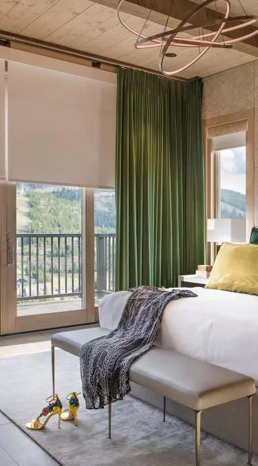 Automated drapes layered with roller shades in bedroom setting