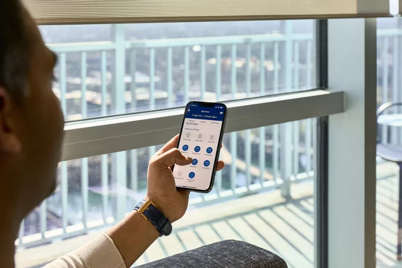 A man using a phone app to control natural lighting scenes with shades.